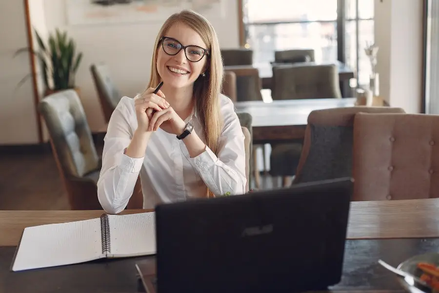 Smiling professional working with laptop and documents symbolising ISO 9001 success through effective quality management and audit preparation.
