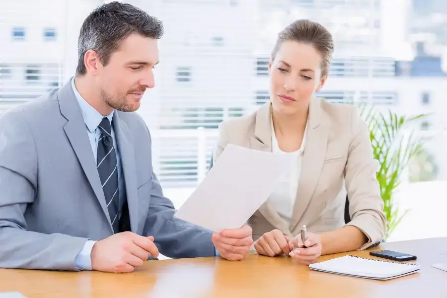 Business professionals reviewing documents during an ISO 9001 checklist meeting in an office setting.