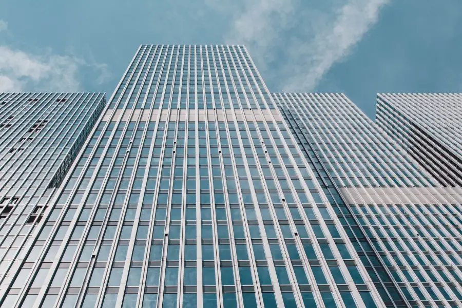 ISO 9001 overview introduction image. Low-angle view of modern glass skyscrapers with vertical lines against a blue sky.